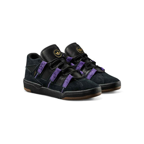 A pair of Adidas  sneakers in black suede and leather with prominent purple elastic straps and a gold logo on the tongue, set against a plain white background.